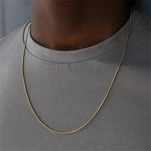 Detailaufnahme einer schmalen goldenen Schlangenkette aus Edelstahl an einem Mann
