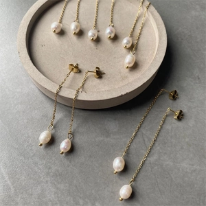 Long gold chain earrings with drop freshwater pearls on gray stone background