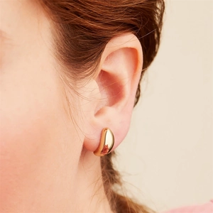 Gros plan de boucles d'oreilles incurvées dorées minimalistes portées par un mannequin