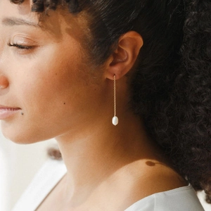 Long gold chain drop earrings with white pearl pendant worn by female model