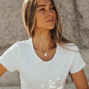 Collier minimaliste à pendentif rectangulaire doré porté sur un t-shirt blanc