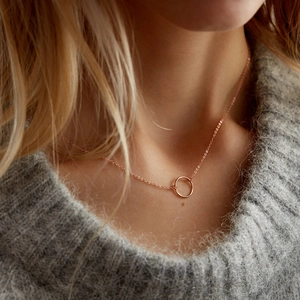 Rose gold round circle pendant necklace worn by a model on a grey sweater