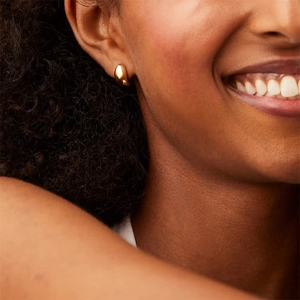 Gros plan de boucles d'oreilles gouttes dorées polies portées sur l'oreille au fini lisse