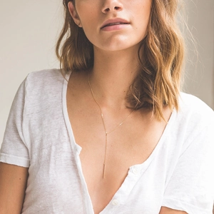 Gros plan d'un collier lasso en acier doré avec pendentif barre minimaliste pour femme