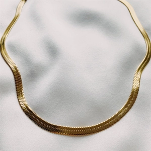 Detailopname van de gouden platte slangenketting op een witte zijden stoffen achtergrond