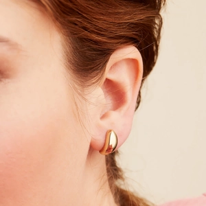 Gros plan de boucles d'oreilles gouttes dorées polies portées par un mannequin chic