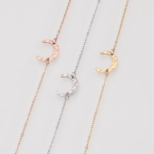 Detail of hammered crescent moon pendants in gold, silver, and rose gold on thin chains