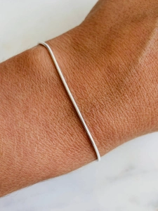 Detail van een dunne zilveren slangenarmband om de pols op een marmeren ondergrond