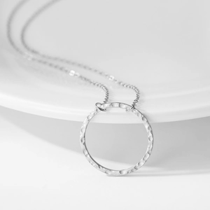 Textured round pendant necklace in stainless steel on white ceramic plate background