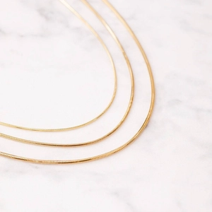 Detailopname van drie goudvergulde slangenketting armbanden op wit marmeren achtergrond