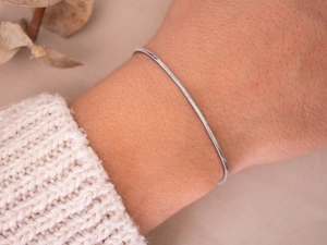 Close-up van een zilveren slangenketting armband om de pols gedragen met een gebreide trui