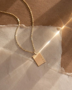 Gros plan du pendentif rectangulaire doré avec dates gravées et texture métal brossé