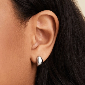 Détail macro d'une boucle d'oreille goutte en argent poli portée par un mannequin