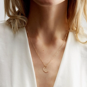 Detail of a gold crescent moon pendant featuring a unique hammered texture on a fine chain