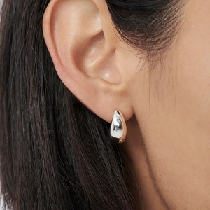 Gros plan d'une boucle d'oreille goutte en argent poli portée par un mannequin chic