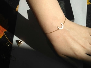 Detail of a minimalist gold crescent moon pendant on a delicate chain worn on wrist