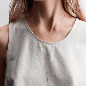 Gros plan d'un collier en Y minimaliste en or rose avec un pendentif barre verticale fine