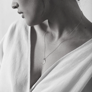 Artistic black and white photo of a crescent moon necklace with hammered metal texture