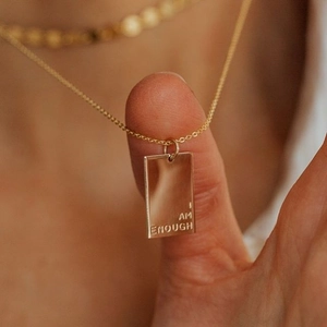 Gros plan du pendentif rectangulaire doré gravé I AM ENOUGH sur une chaîne fine