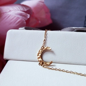 Elegant gold crescent moon necklace with hammered texture on a leather jewelry box