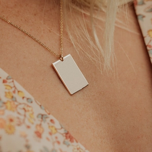 Gros plan d'un pendentif rectangulaire doré poli sur une chaîne fine portée par un modèle