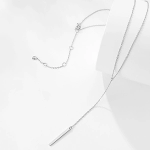 Détail d'un collier minimaliste argenté avec pendentif barre verticale et chaîne réglable