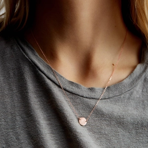 Close-up of minimalist rose gold necklace with a round pendant on a model wearing grey