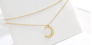 Macro detail of golden crescent moon pendant featuring a unique hammered metal texture