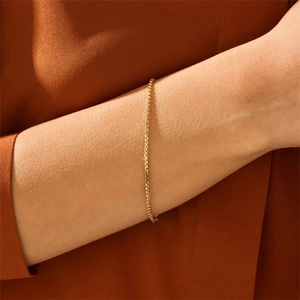 Minimalist golden stainless steel box chain bracelet worn on wrist over textured fabric