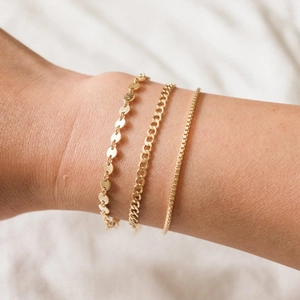 Close-up of layered gold bracelets featuring curb, box, and sequin link designs