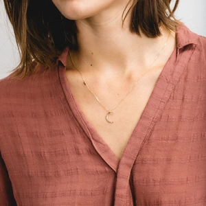 Close-up of a minimalist golden crescent moon pendant necklace worn on a model