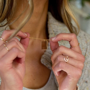 Collier minimaliste à pendentif carré doré et ensemble de bagues portés par un modèle