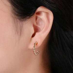 Detailed close-up of a golden twisted C-shaped earring on a female ear model