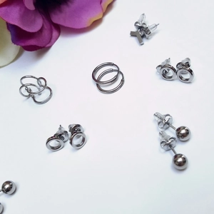 Minimalist silver stainless steel earring set featuring hoops, studs, and ear cuffs on white