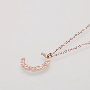 Detailed macro view of a rose gold moon pendant with hand-hammered texture on an O-chain