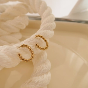 Macro di orecchini a cerchio a C intrecciati dorati presentati su una corda di cotone bianco