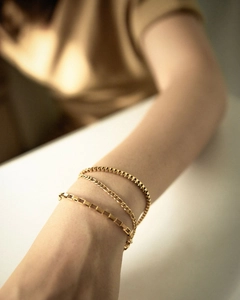 Close-up of a gold-plated box chain and curb link bracelet set on a model wrist