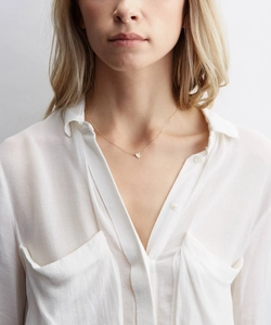 Detail of a minimalist gold heart pendant necklace worn on a woman with a white shirt