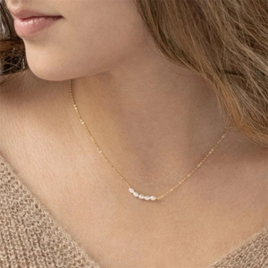 Minimalist gold chain necklace with five freshwater pearls on a female model