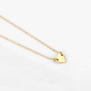 Close-up of polished gold heart pendant necklace on a minimalist white background