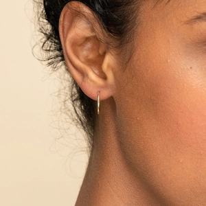 Petites créoles minimalistes en or et acier inoxydable poli portées sur le lobe d'oreille