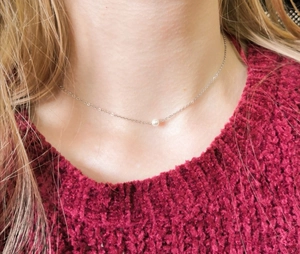 Nahaufnahme einer Perlenkette aus Edelstahl an einem Model mit rotem Strickpullover