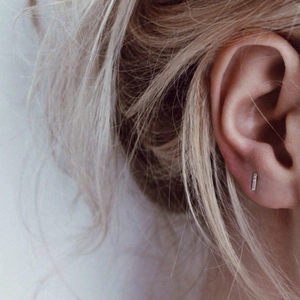 Minimalist silver geometric bar stud earrings in stainless steel on ear lobe
