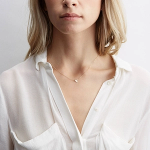 Minimalist gold heart pendant necklace for women worn with a white blouse on grey background