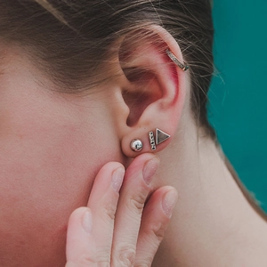 Close-up of minimalist silver geometric stud earrings and crystal ear cuff on model