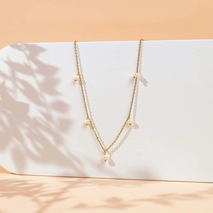 Detail of gold chain necklace with five white pearls against a soft aesthetic shadow background