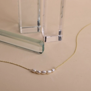 Macro view of five white oval freshwater pearls on a delicate gold link chain