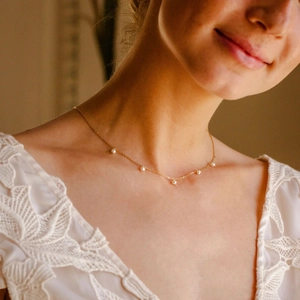 Elegant gold necklace with five pearls on a model wearing a white lace top