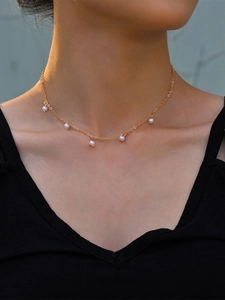 Close-up of a gold necklace featuring five white pearls worn by a model in a black V-neck top