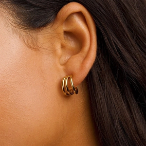 Close-up of a model wearing triple-layered gold curved C-shape hoop earrings in polished finish